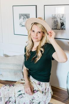 a woman sitting on the floor wearing a flowered skirt and a hat with her hands behind her head