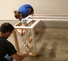 two people working on a table in the middle of a room with unfinished wood framing