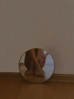 a person's legs are reflected in a round mirror on the floor next to a wall