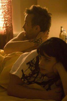 a man and woman laying in bed next to each other with tattoos on their arms