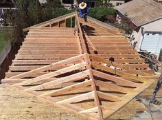 a man standing on top of a wooden roof in the middle of a house under construction