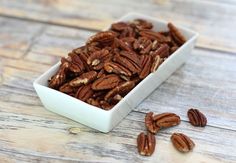 a white bowl filled with pecans on top of a wooden table