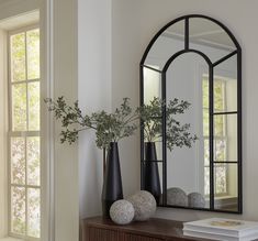 two vases with flowers are sitting on a table next to a mirror and a book