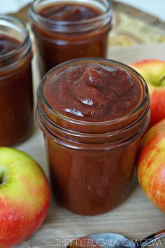 three jars filled with apple butter sitting on top of a table next to some apples