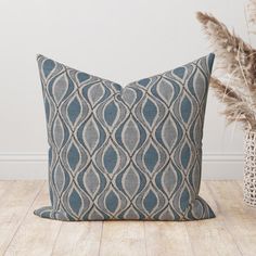 a blue and white pillow sitting on top of a wooden floor next to a potted plant