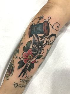 a person with a tattoo on their arm holding a spool of thread and scissors