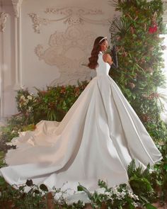 a woman in a white wedding dress standing next to a christmas tree with greenery