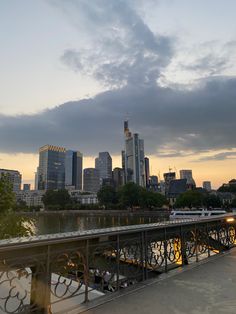 the city skyline is lit up at night as people walk on a bridge over water