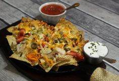 nachos and salsa on a black plate with a small bowl of dipping sauce