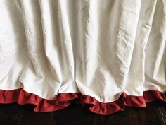 a white bed with red ruffles on it's sides and a wooden floor