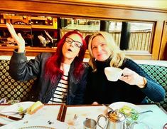 two women sitting at a table with plates and cups in front of them, posing for the camera