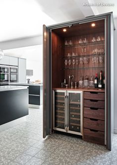 an open cabinet with wine glasses and bottles in it on the floor next to a counter