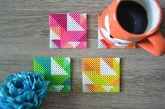 four square coasters with different designs on them and a blue flower next to it