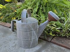 a watering can sitting on the ground next to some plants