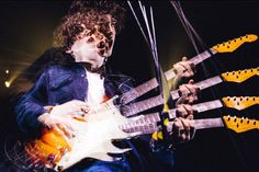 a man with curly hair playing an electric guitar in front of other guitars on stage