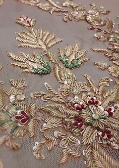 gold embroidered fabric with red and green flowers on grey background, close - up photo