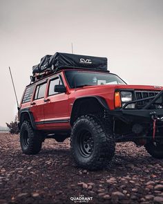 a red four door suv parked on top of a rocky field