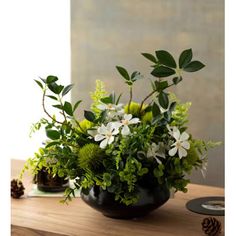 a black vase filled with white and green flowers on top of a wooden table next to a pine cone