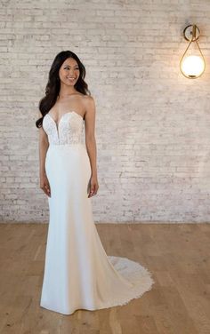 a woman in a white wedding dress standing on a wooden floor next to a brick wall