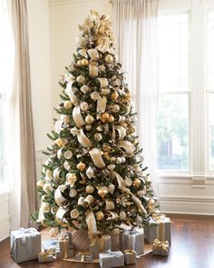 a decorated christmas tree with gold and silver ornaments on it's branches, surrounded by presents