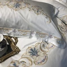 a white bed topped with pillows and a cup of coffee next to an ornately decorated pillow