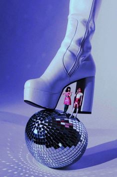 a pair of white high heeled shoes on top of a disco ball in front of a purple background