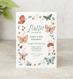 a white birthday card with butterflies and flowers on it, sitting next to a potted plant