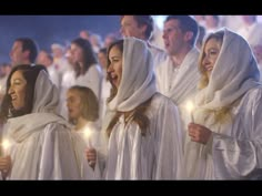 a group of people standing next to each other with candles in their hands and wearing white robes