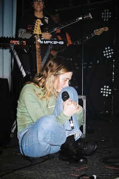 a woman sitting on the ground with a microphone in her hand and other musicians behind her