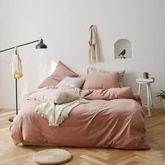 an unmade bed with pink sheets and pillows in a white room next to a wooden floor