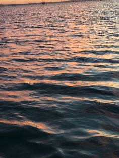 the sun is setting over the ocean with sailboats in the distance and one boat out on the water