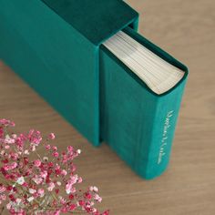 an open book sitting on top of a wooden table next to a vase with pink flowers