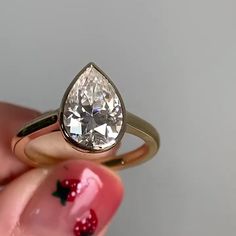 a woman's hand holding an engagement ring with a pear shaped diamond