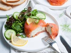 a white plate topped with salmon and cucumbers next to slices of lemon wedges