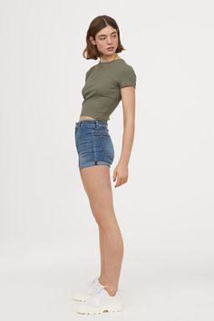 a young woman is posing for the camera wearing shorts and a t - shirt with an olive green crop top