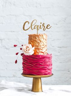 a pink and gold cake with the name claire on top, sitting on a table