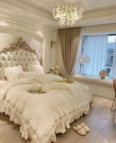 a white bed sitting in a bedroom next to a window with curtains and chandelier