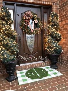 the front door is decorated for christmas with wreaths and potted trees on it