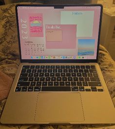 an open laptop computer sitting on top of a bed next to a pink wallpaper