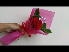 someone is holding a pink box with a red rose on it and ribbon tied around the top