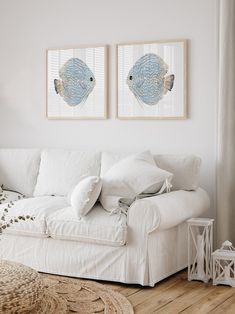 two paintings hang on the wall above a white couch in a room with wood floors