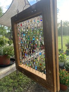 an old stained glass window hanging from a wooden frame in the grass with potted plants behind it