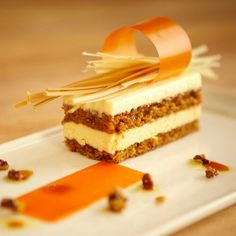 a piece of cake on a white plate with an orange ribbon and some nuts around it