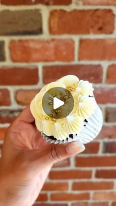 a person holding up a cupcake in front of a brick wall