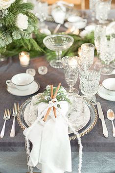 the table is set with white dishes and silverware, greenery, and candles