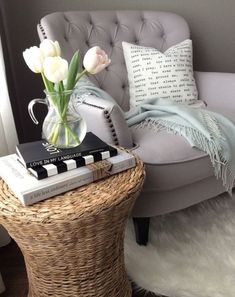 a wicker table topped with a vase filled with white flowers next to a gray chair