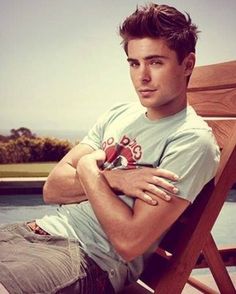 a man sitting on top of a wooden chair next to a pool with his arms crossed