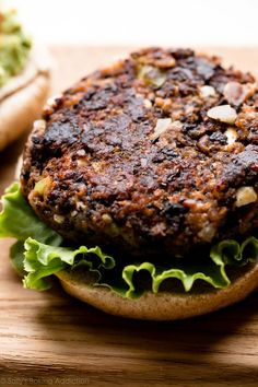 a hamburger with lettuce and other toppings sitting on a wooden cutting board