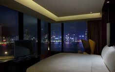 a bed in a bedroom next to a large window with city lights on the other side