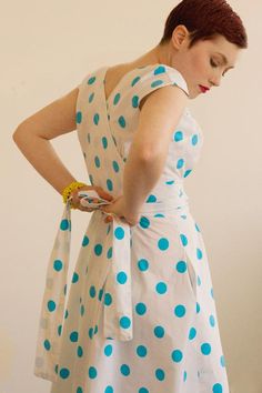 a woman in a polka dot dress is holding her hand on her hip and looking down